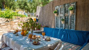 An outdoor dining area with a table set for two, surrounded by stone walls and potted plants. - Villa Eirini Ionian Home (Paxos)