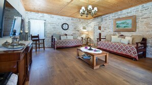 A cozy room with a wooden ceiling, stone walls, a sofa, a chair, a coffee table, and a painting. - Villa Eirini Ionian Home (Paxos)