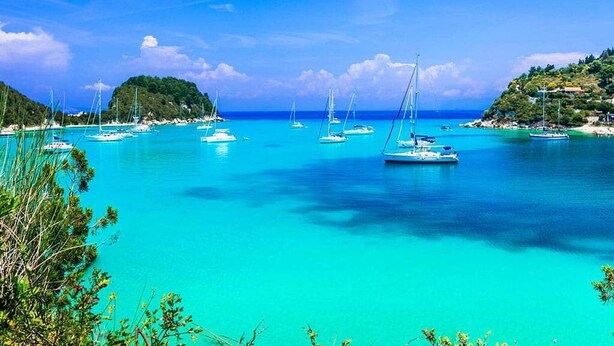 A coastal scene with clear turquoise waters, boats, and a hilly landscape. - Villa Eirini Ionian Home (Paxos)