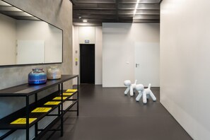 Welcome to our hotel, where sleek lines and modern design create a sophisticated atmosphere. The reception area features a long desk with a mirror and decorative accents, leading to a door and elevator beyond.
