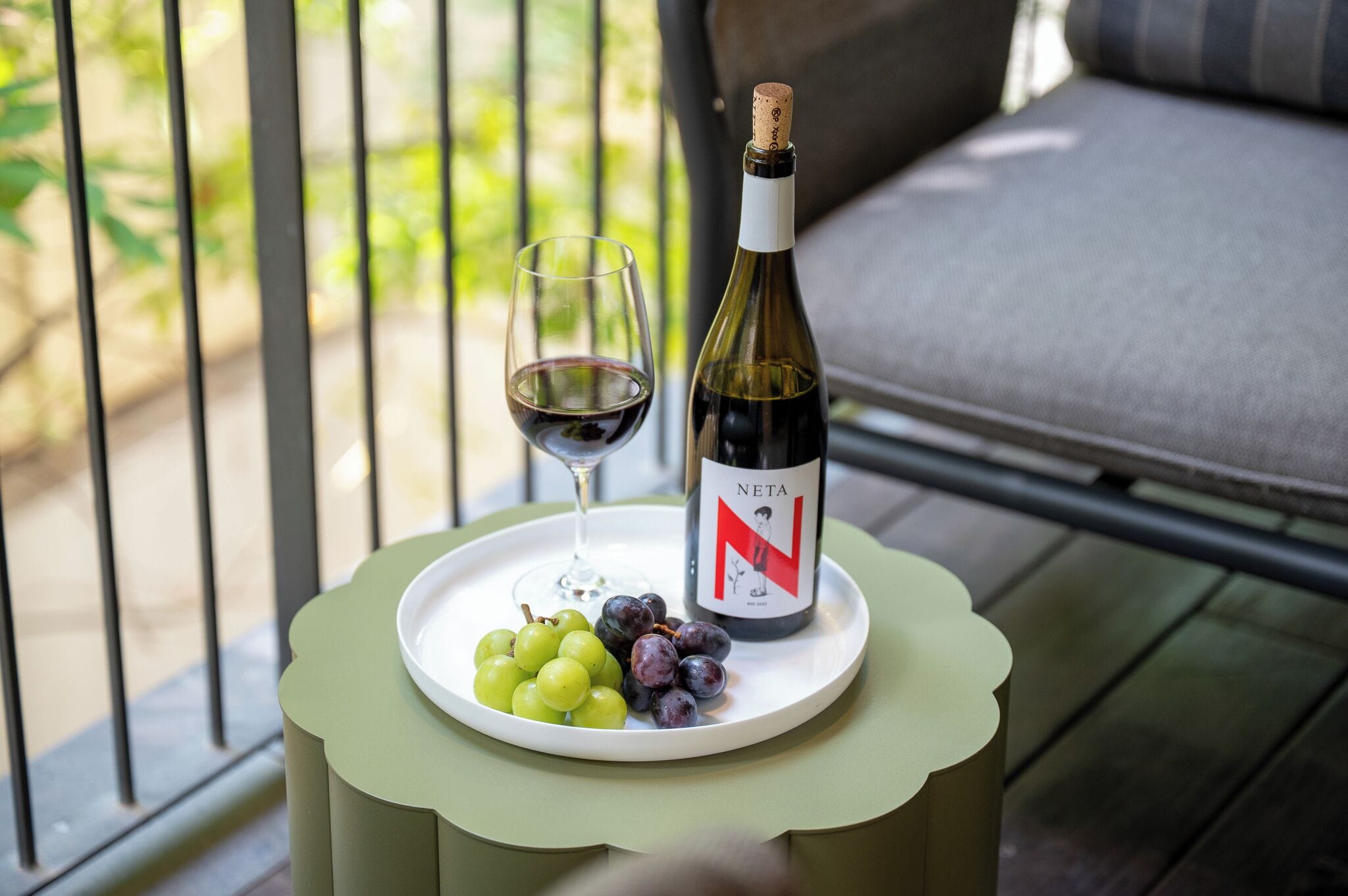 A bottle of wine, a glass of red wine, and a plate with grapes on a table.