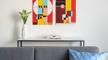 A living room with a gray sofa, a white vase with green plants, and two abstract paintings on the wall.