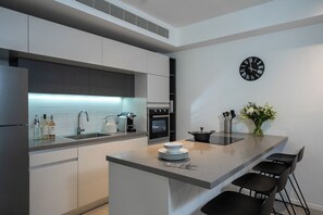 A modern kitchen with white cabinets, a built-in oven, a sink, and a bar area with chairs. - master Shenkin (Tel Aviv)