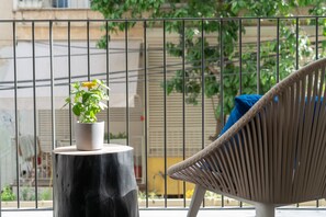 Relax on the balcony with a view of the surrounding greenery, featuring a wicker chair and a potted plant.