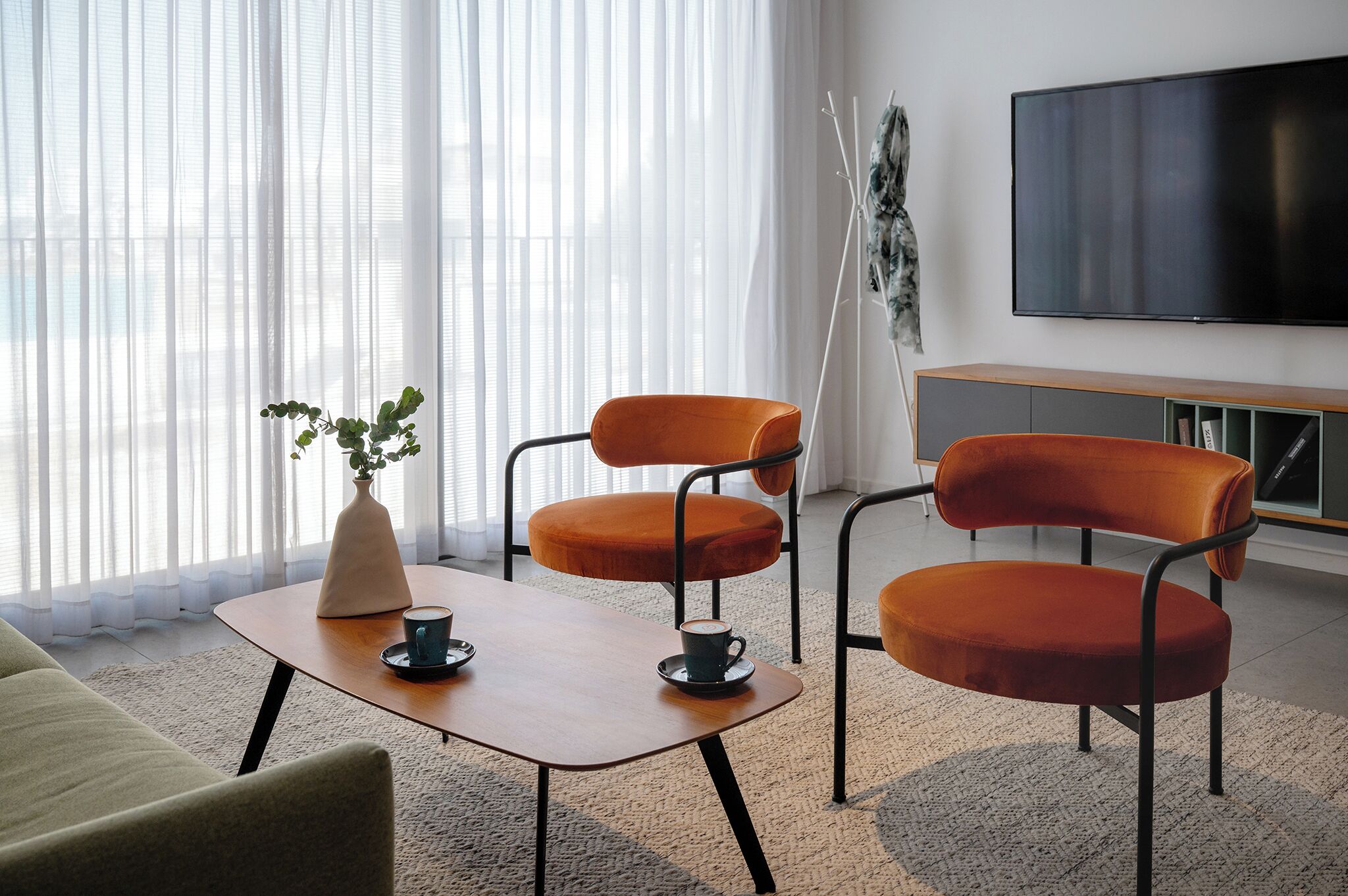 Una sala moderna con un sofá, dos sillones naranja, una mesita de centro, un televisor y una planta.