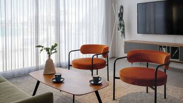 Uma sala de estar moderna com um sofá, duas poltronas laranja, uma mesa de centro, uma televisão e uma planta.