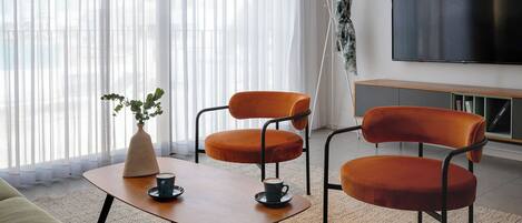 Una sala moderna con un sofá, dos sillones naranja, una mesita de centro, un televisor y una planta.