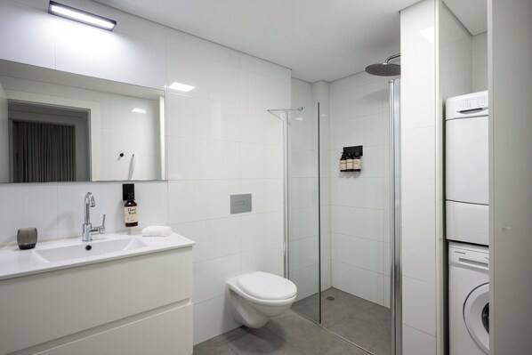 Un baño moderno con ducha de vidrio, un lavamanos blanco y un inodoro.