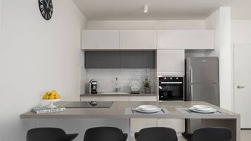 A modern kitchen with white cabinets, a stainless steel refrigerator, a built-in oven, and a central island with bar stools.