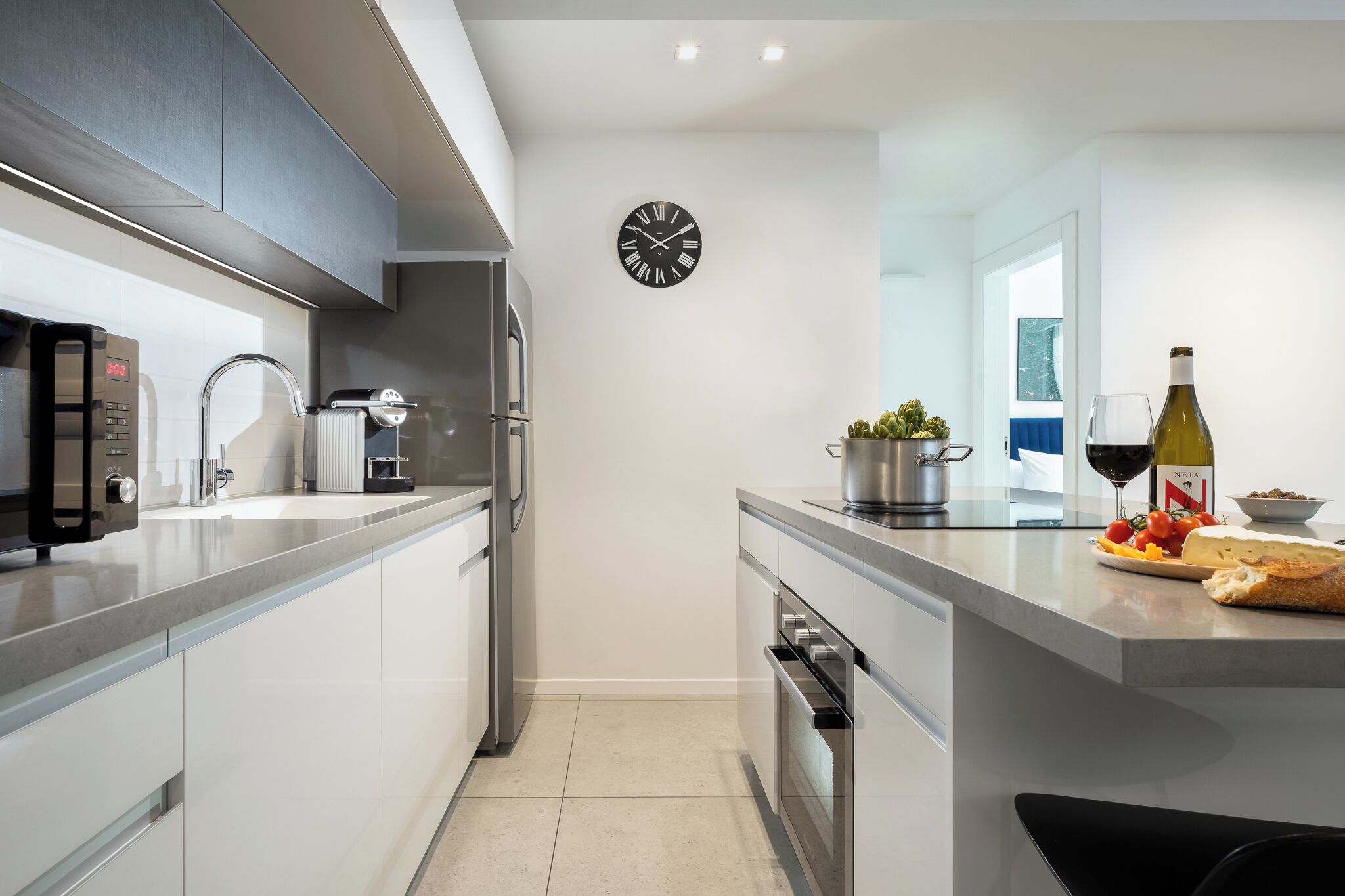 A modern kitchen with a clock, stainless appliances, and a counter with food and drink.