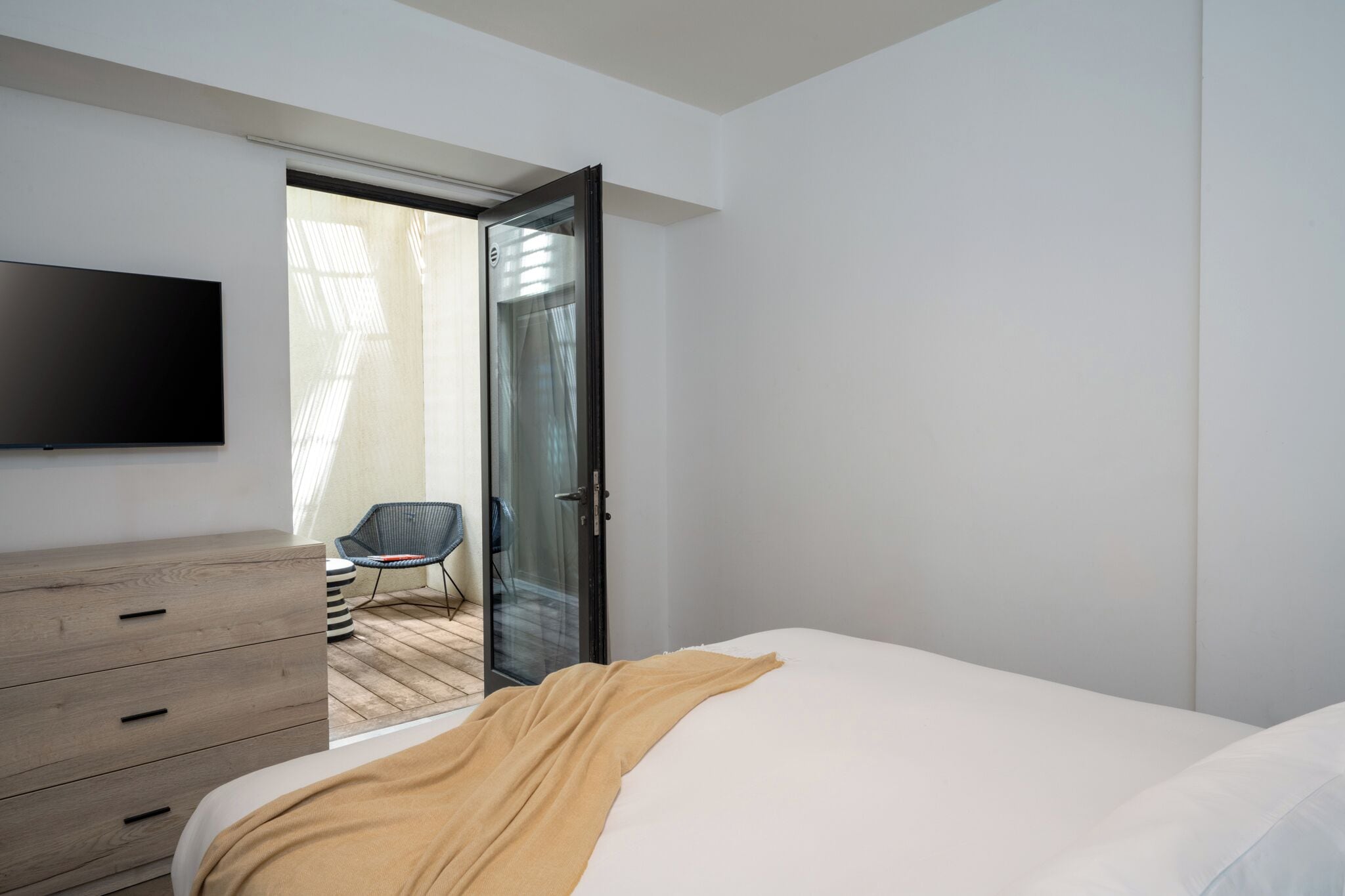 A bedroom with a bed, a TV mounted on the wall, a wooden dresser, and a chair.