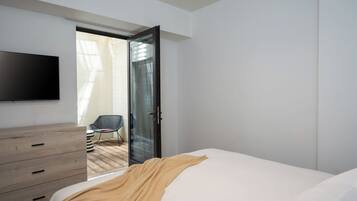 A bedroom with a bed, a TV mounted on the wall, a wooden dresser, and a chair.