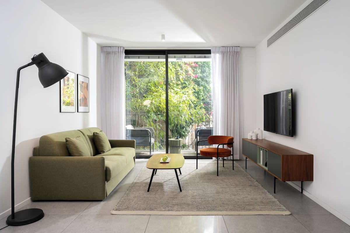 Ein modernes Wohnzimmer mit einer Couch, einem Couchtisch, einem Fernseher und Blick durch eine Schiebetür.
