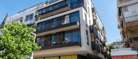 A modern multi-story building with balconies, large windows, and a storefront with yellow panels.