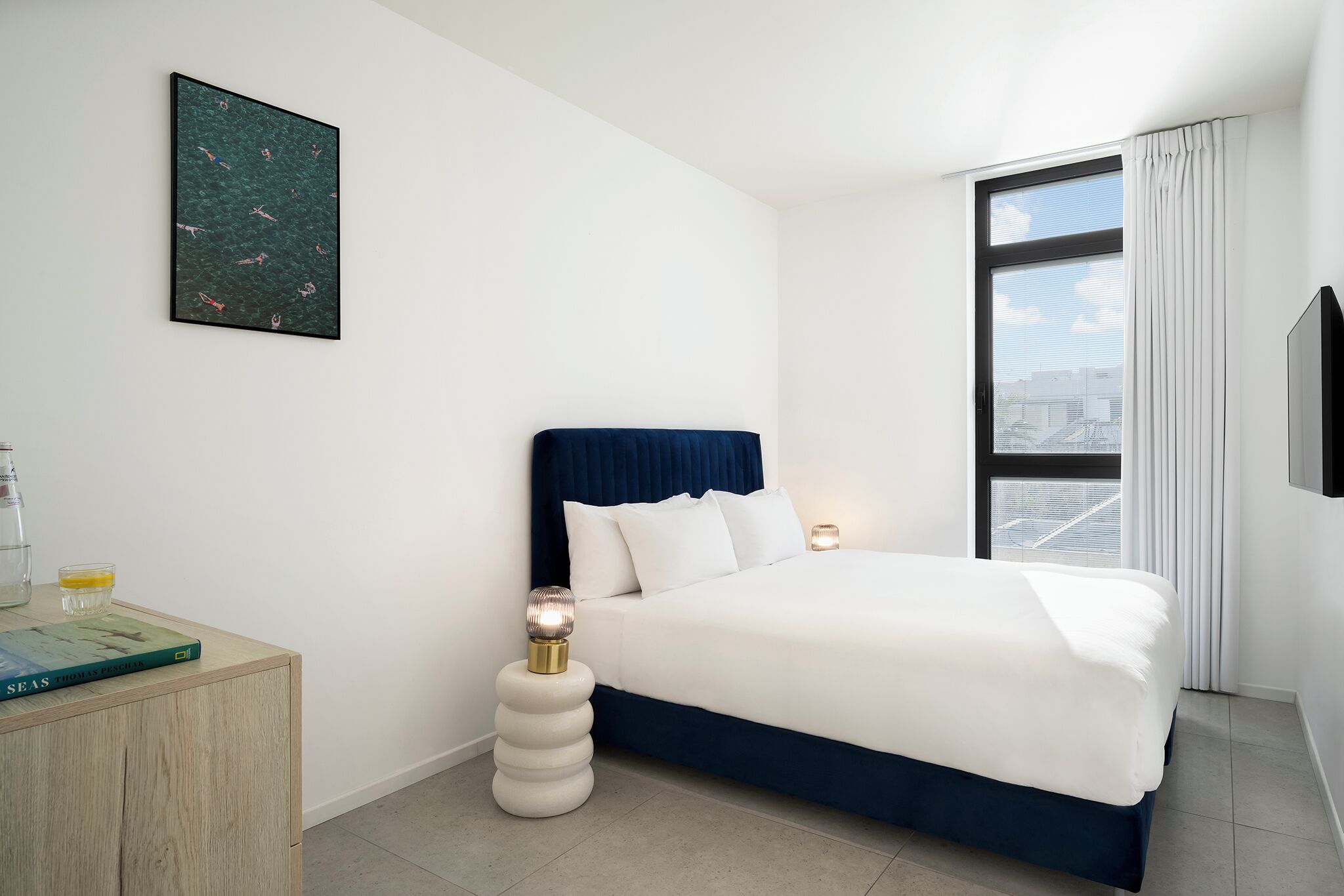 Ein modernes Hotelzimmer mit Bett, Nachttisch, Vorhängen und Blick auf die Stadt.