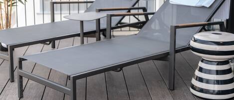 A sun lounger with a metal frame and a cushion, a small table, and a striped stool on a wooden deck.