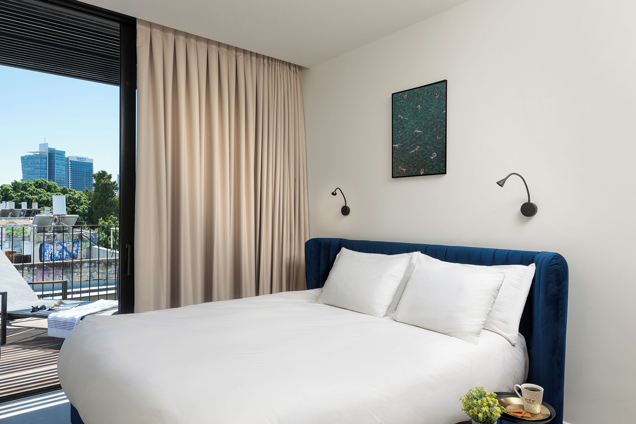 Habitación de hotel con una cama grande, vistas a la ciudad y un balcón con mobiliario exterior.