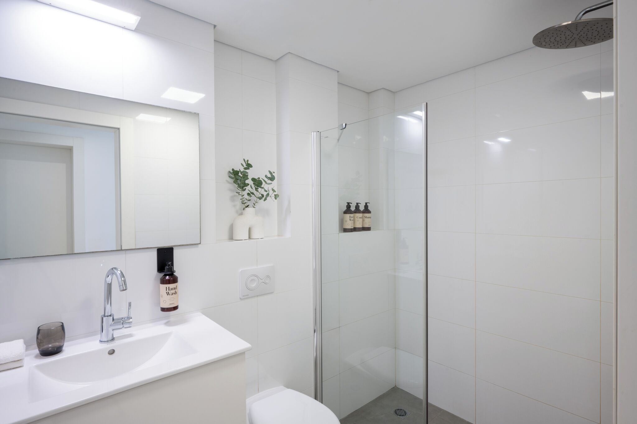 A modern bathroom with a white sink, a glass shower enclosure, and a mirror above the sink.