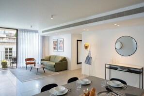 A modern living room with a dining area, a sofa, a coffee table, and a dining table set for two. - master Shenkin (Tel Aviv)