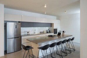 A modern kitchen with a central island, bar stools, a refrigerator, and a coffee machine. - master Shenkin (Tel Aviv)
