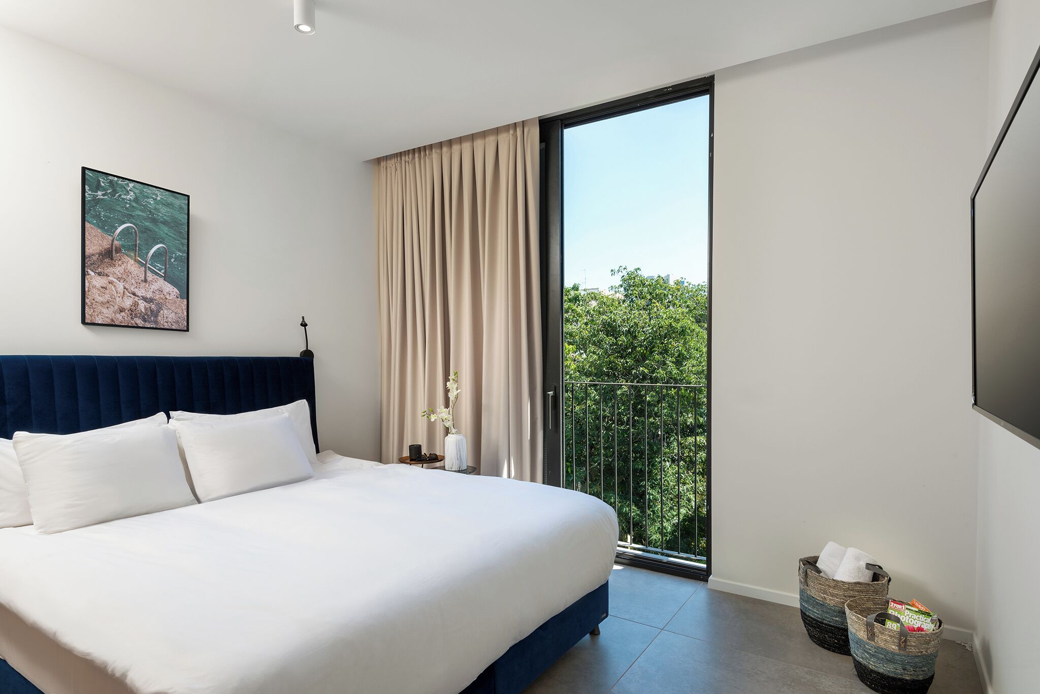 Een moderne slaapkamer met een groot bed, uitzicht op groen via een balkon en een schilderij aan de muur.