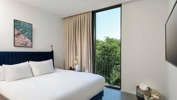 Une chambre moderne avec un grand lit, une vue sur la verdure depuis un balcon et un tableau accroché au mur.