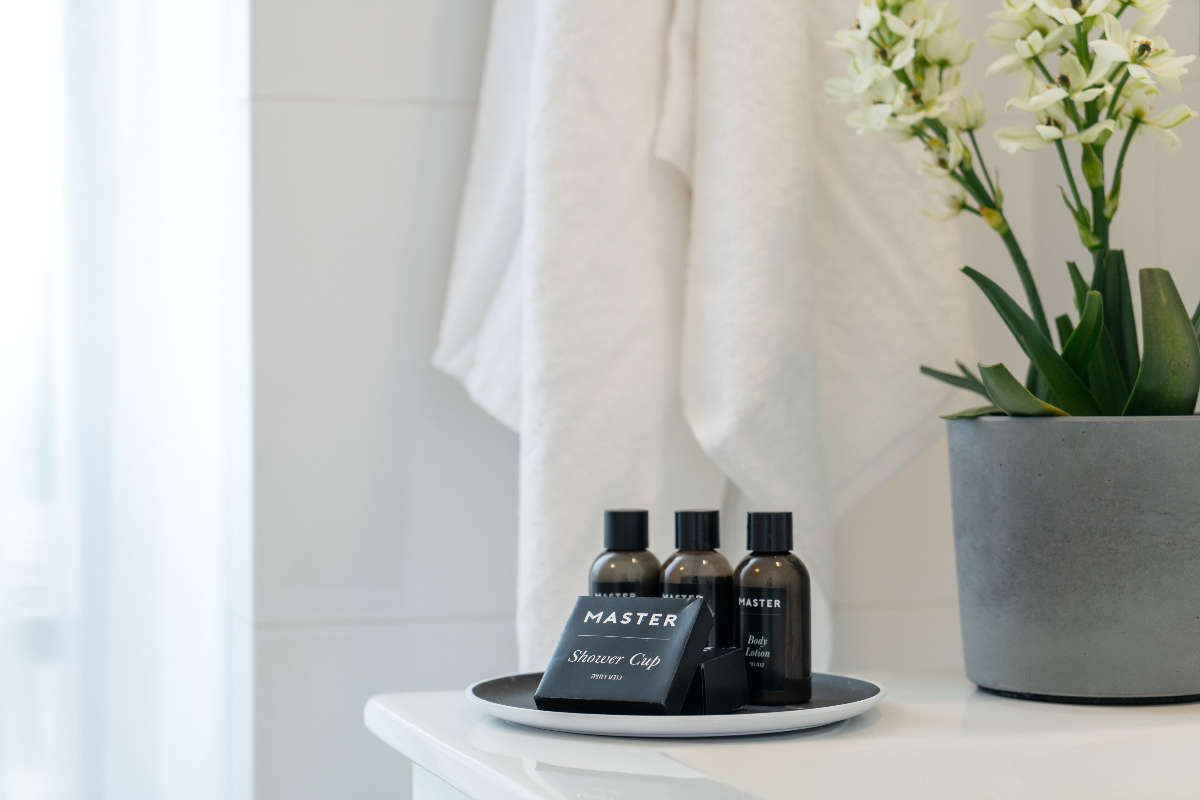 A bathroom counter with a white towel hanging on a towel rack, a potted orchid plant, and three Master Shower Cup bottles.