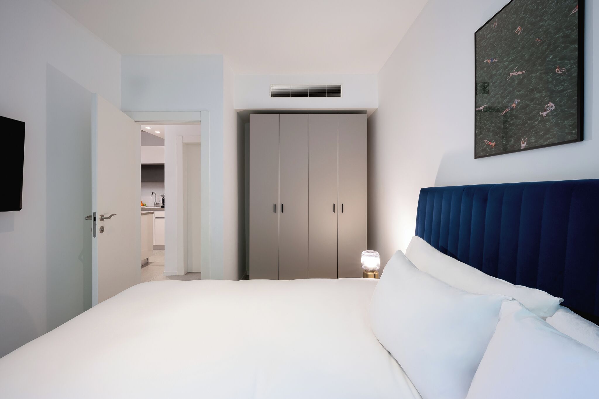 Un dormitorio moderno con cama, armario, lámpara de noche y televisor montado en la pared.