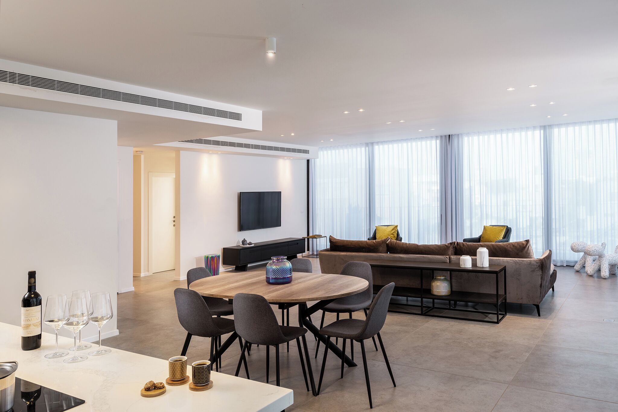 Un salon moderne comprenant un coin repas, un canapé et un téléviseur fixé au mur.