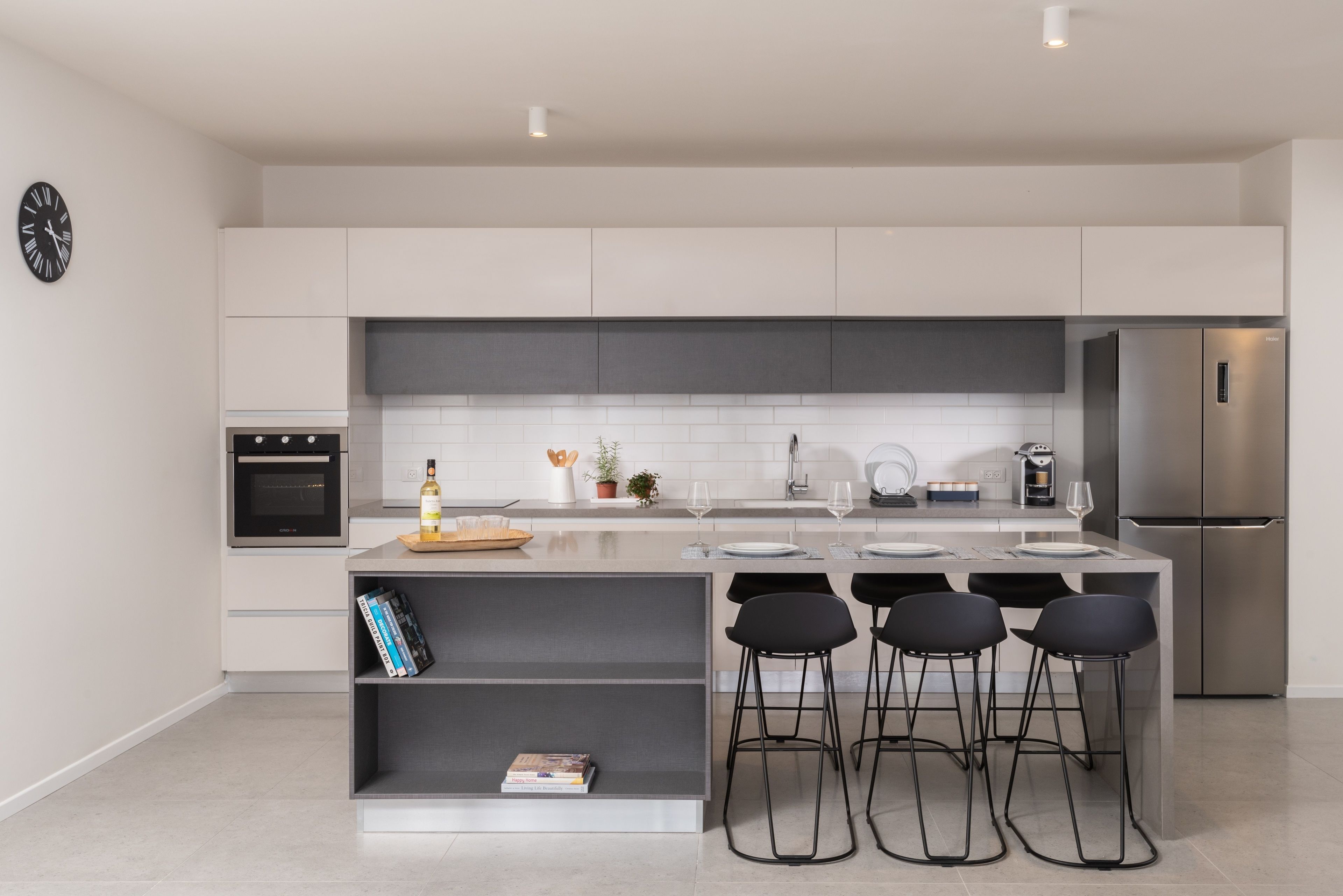 Una cucina moderna con isola centrale, sgabelli da bar, forno integrato e frigorifero in acciaio inossidabile.