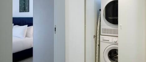 Una habitación de hotel con una cama, una lavadora y una puerta que da a otra habitación.