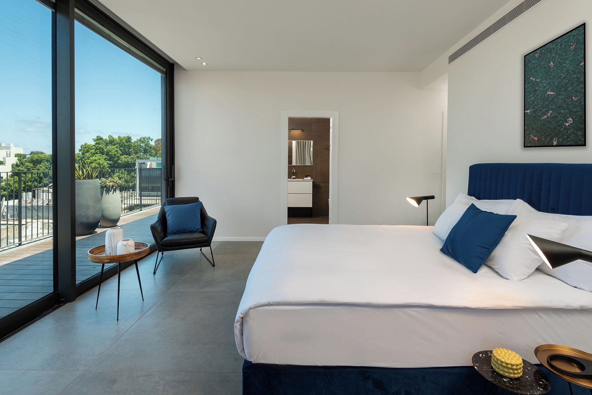 A modern hotel room with a large bed, a seating area, a bathroom, and a balcony with a view.