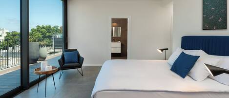 A modern hotel room with a large bed, a seating area, a bathroom, and a balcony with a view.