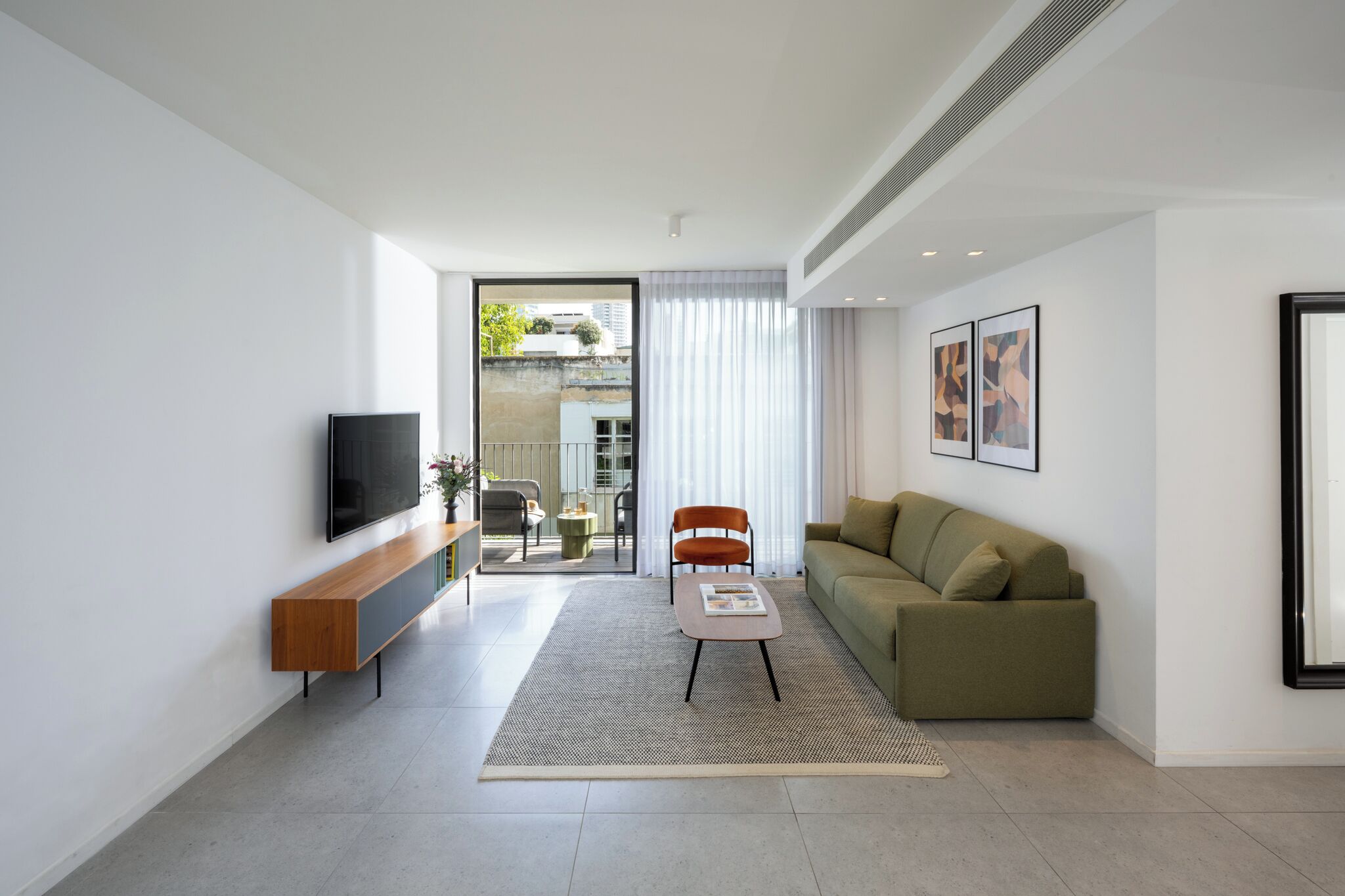 A modern living room with a flat-screen TV, a wooden bench, a green sofa, a coffee table, and a large window with curtains.