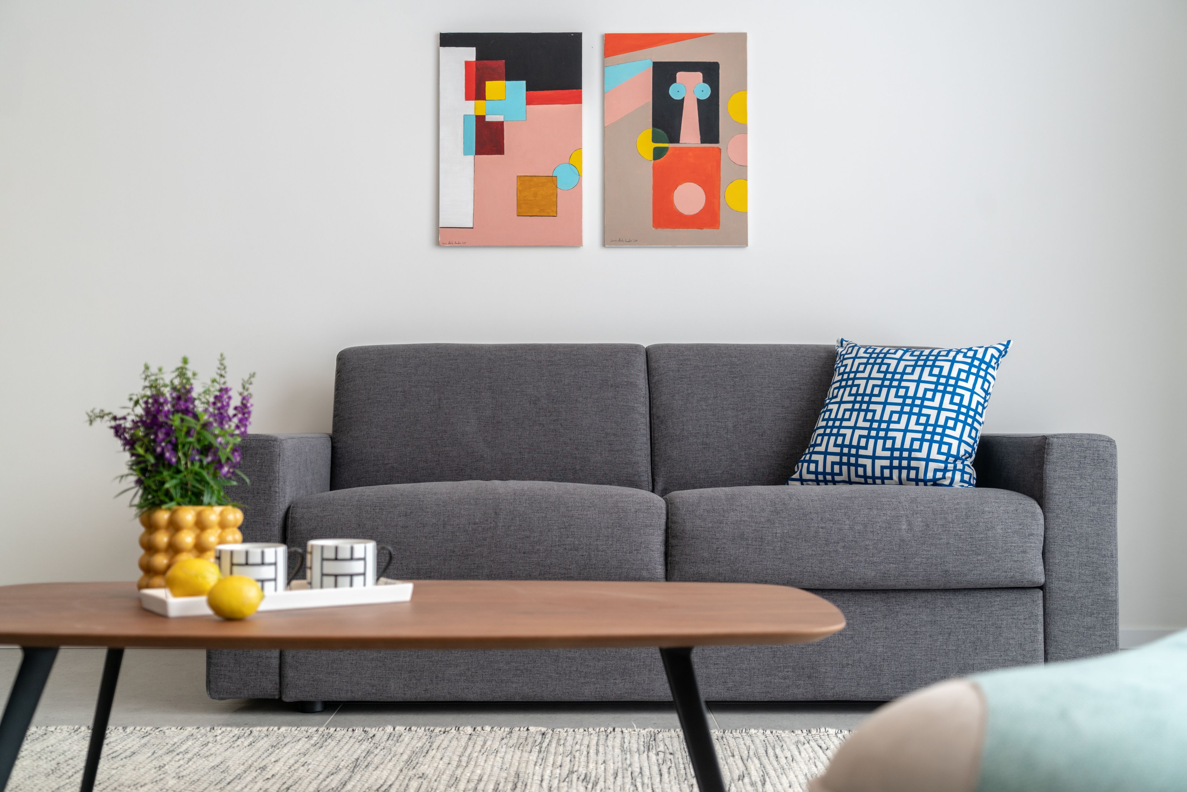 A modern living room with a grey sofa, a patterned pillow, a wooden coffee table, and abstract art on the wall.
