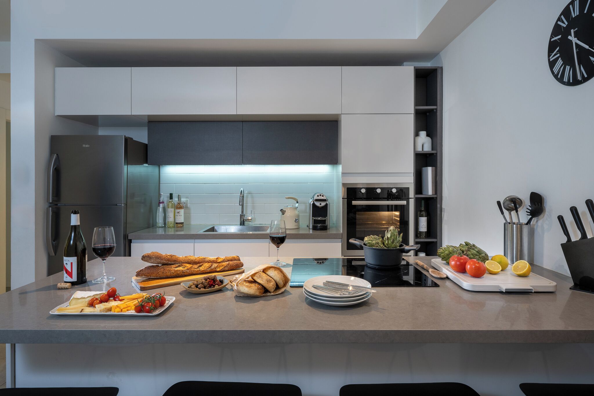 A modern kitchen with a central island, stainless steel appliances, and a clock on the wall.