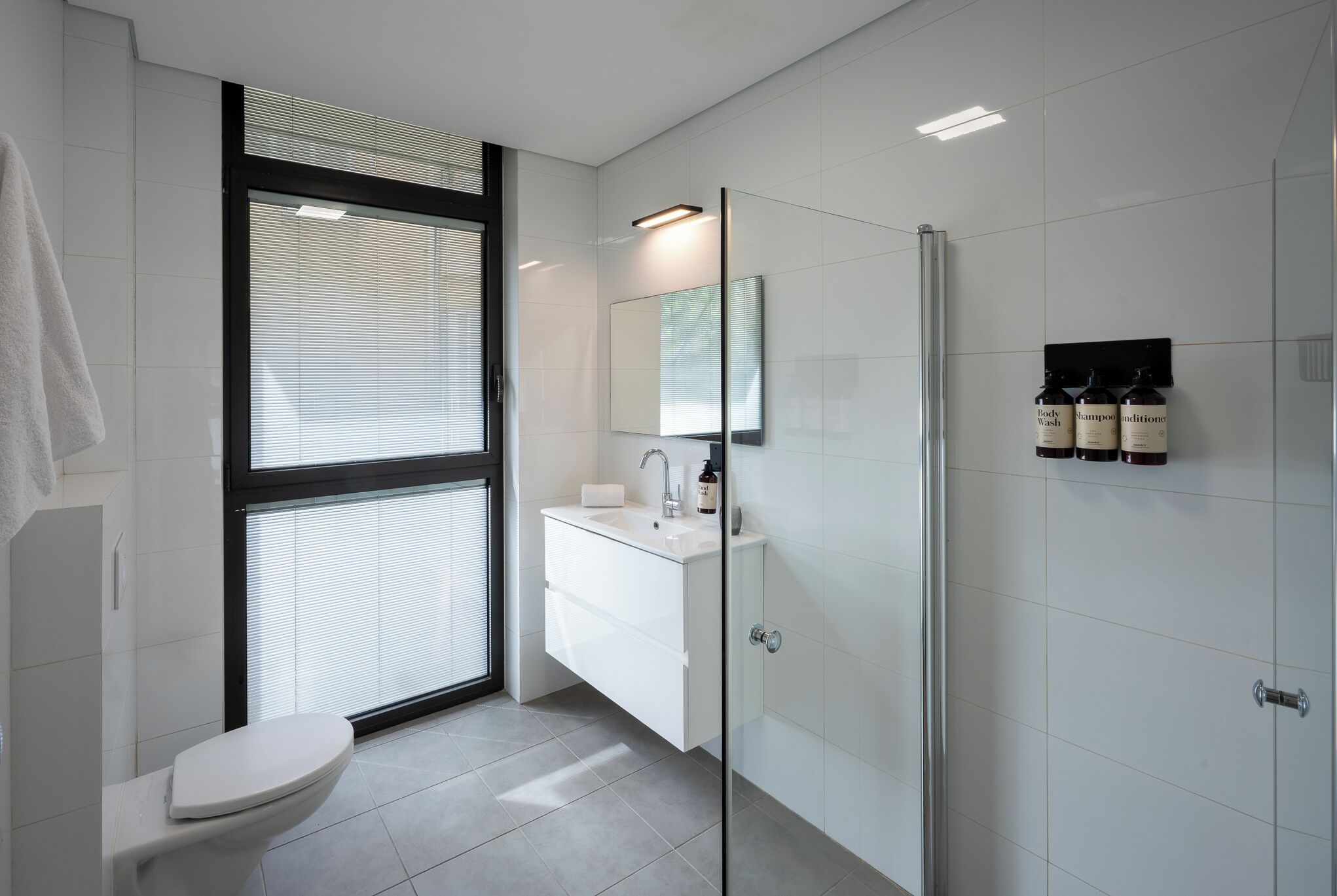 A modern bathroom with a toilet, sink, mirror, and shower.