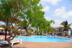 A swimming pool with lounge chairs and umbrellas, surrounded by palm trees and a building with a tiled roof. - Private Self-Catering Apartments (Sal)