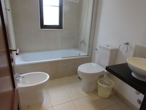 A bathroom with a bathtub, two toilets, a sink, and a window. - Private Self-Catering Apartments (Sal)