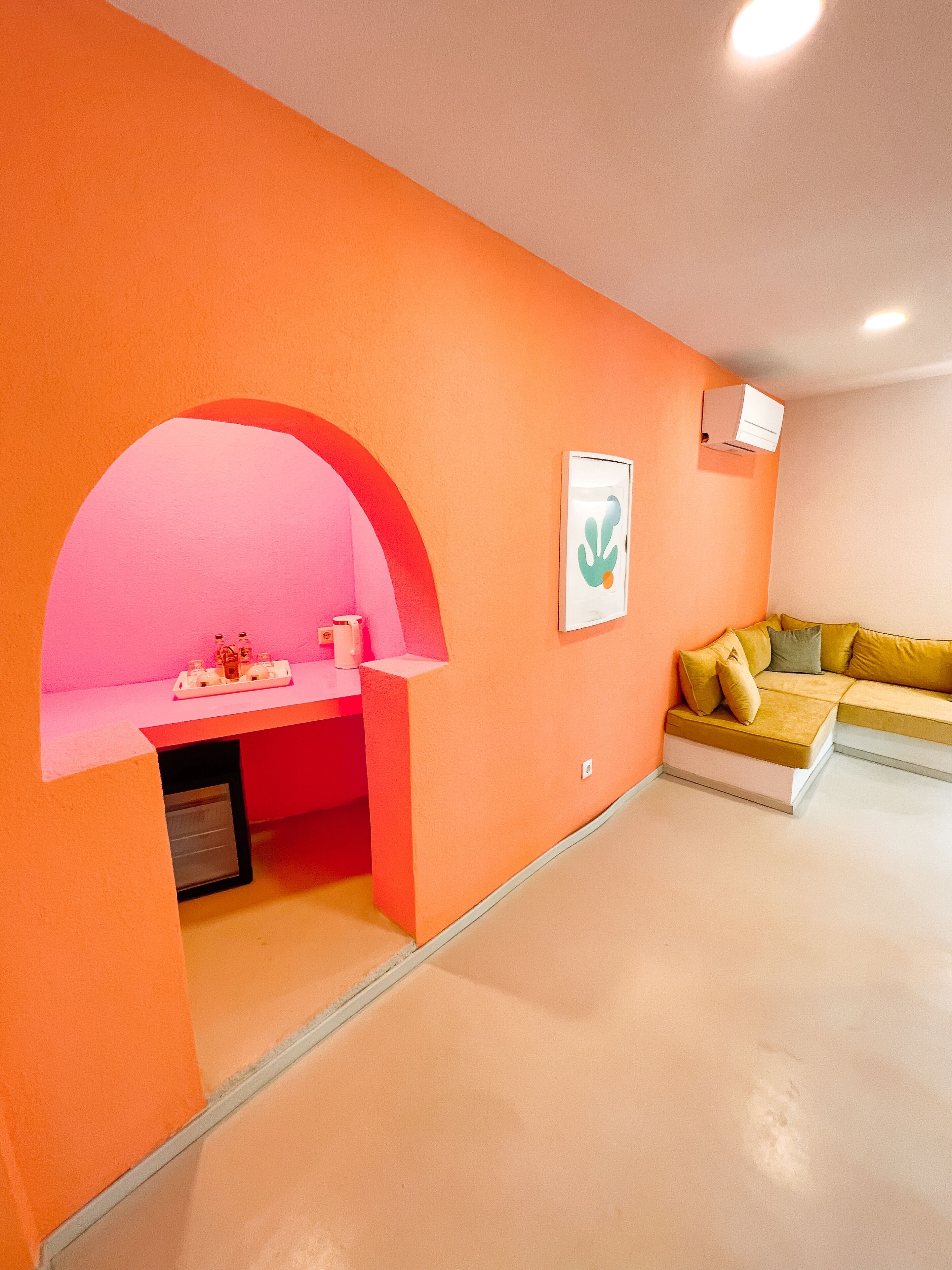 Une pièce avec un mur orange, une arche rose, un canapé jaune et une petite table sur laquelle se trouve un plateau avec divers objets.