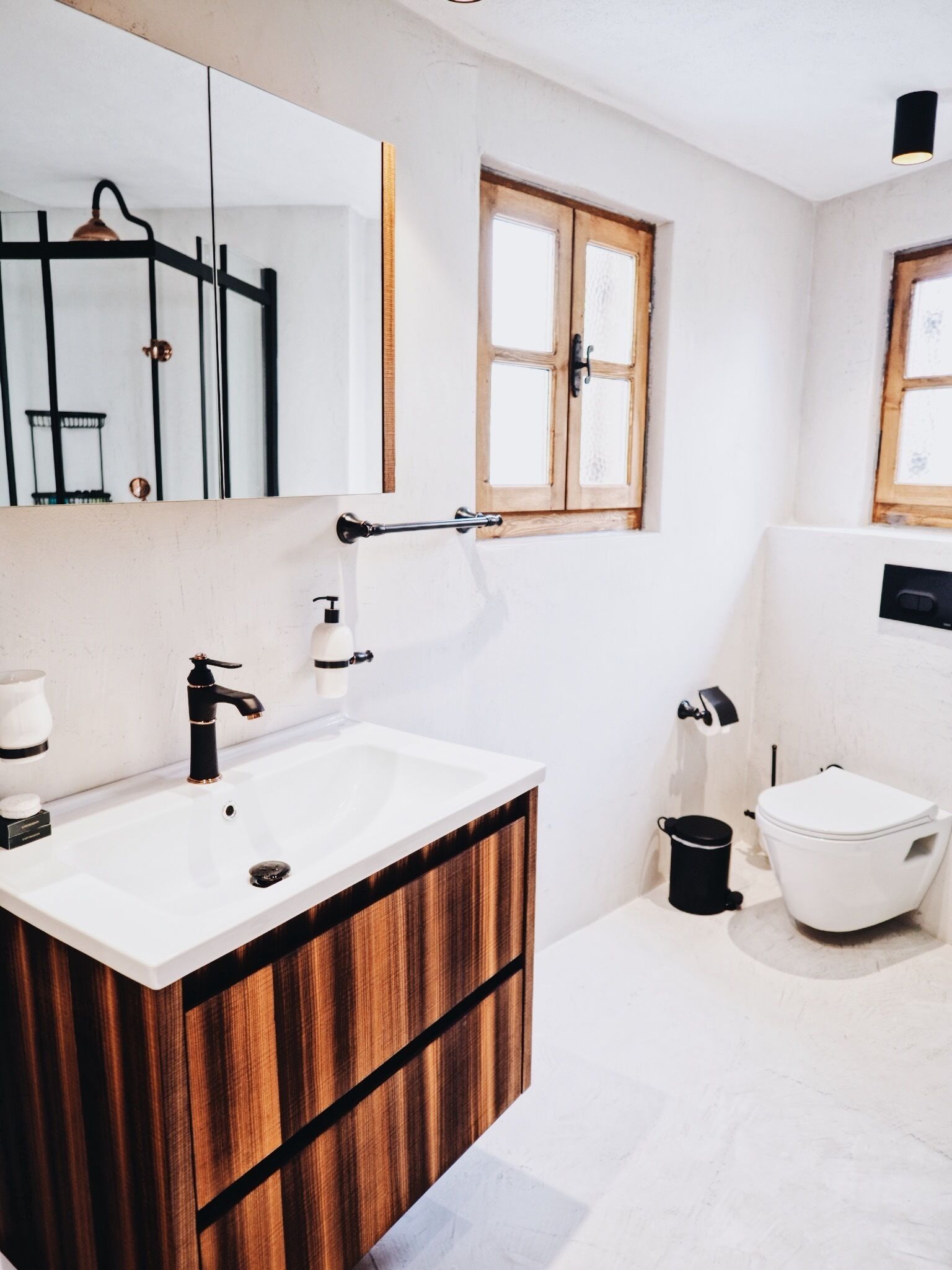 A modern bathroom with a wooden vanity, a white sink, a mirror, and a window.