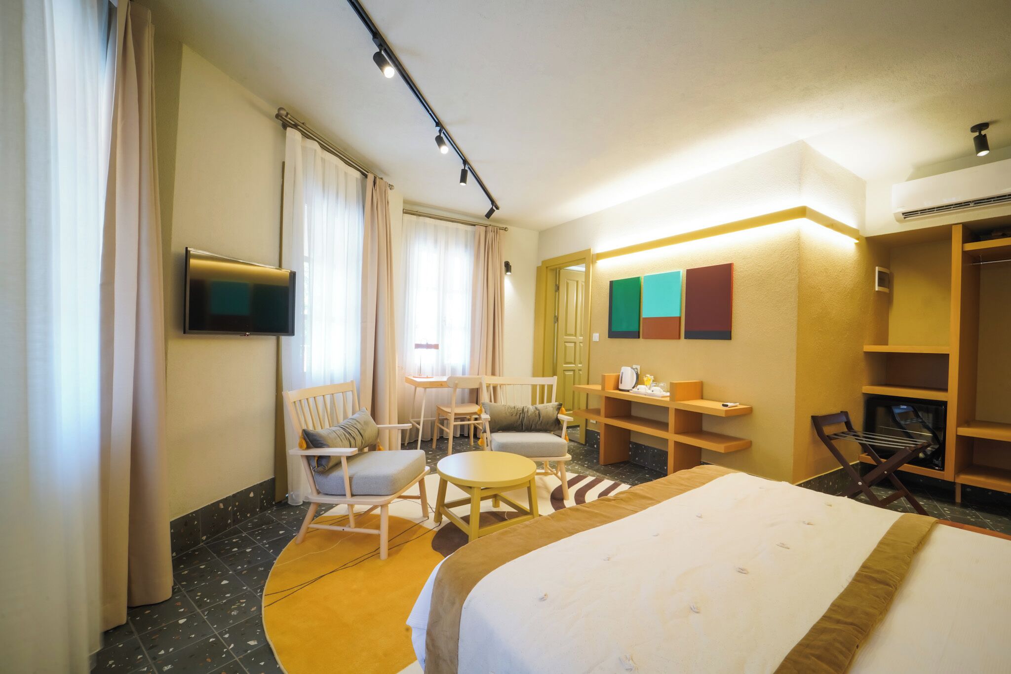 A hotel room with a bed, a TV, a seating area with chairs and a table, and a wardrobe.