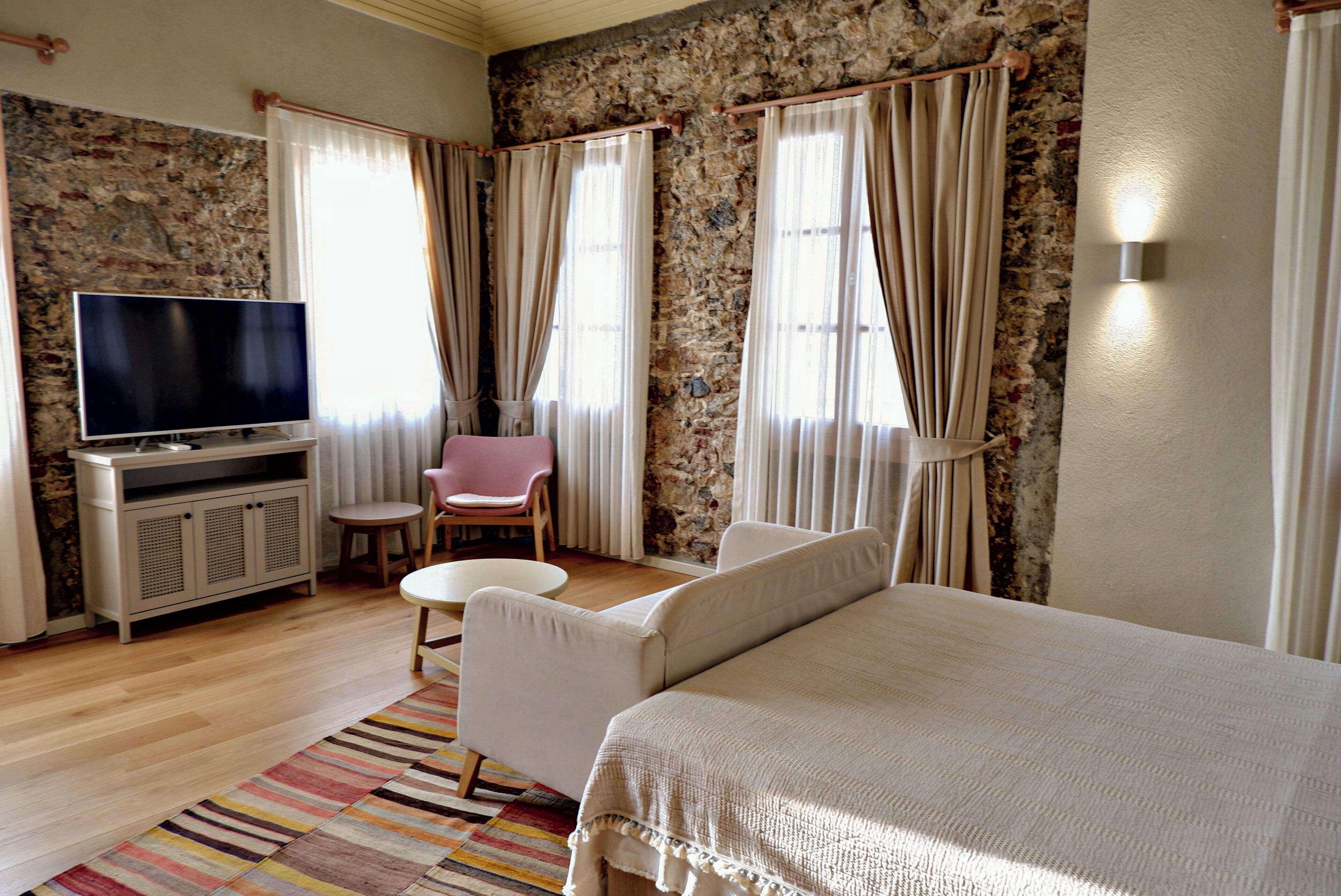 Quarto de hotel com cama, televisão, mesa pequena, cadeira e sofá.