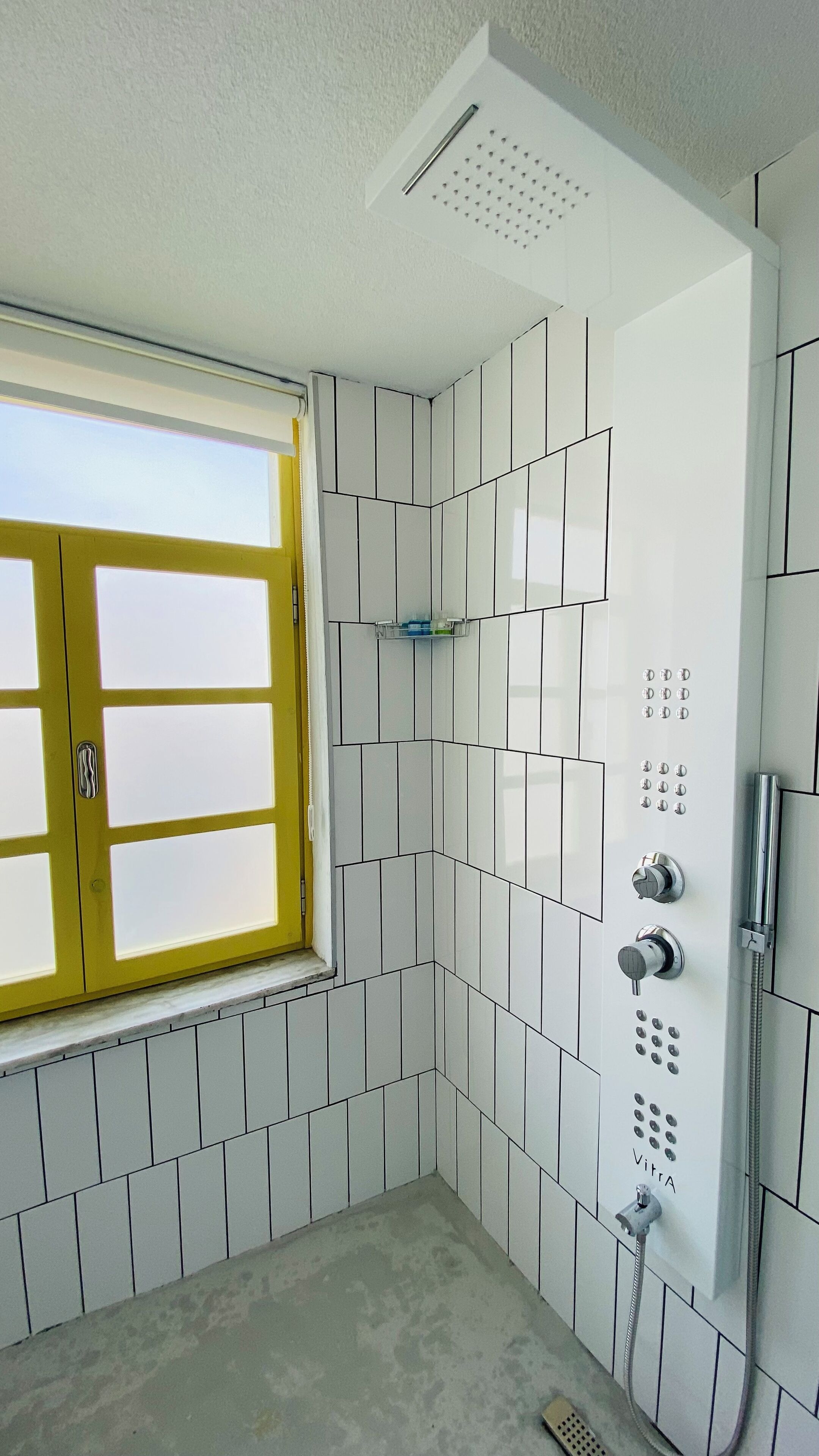 A bathroom with a shower, a window, and a tiled wall.