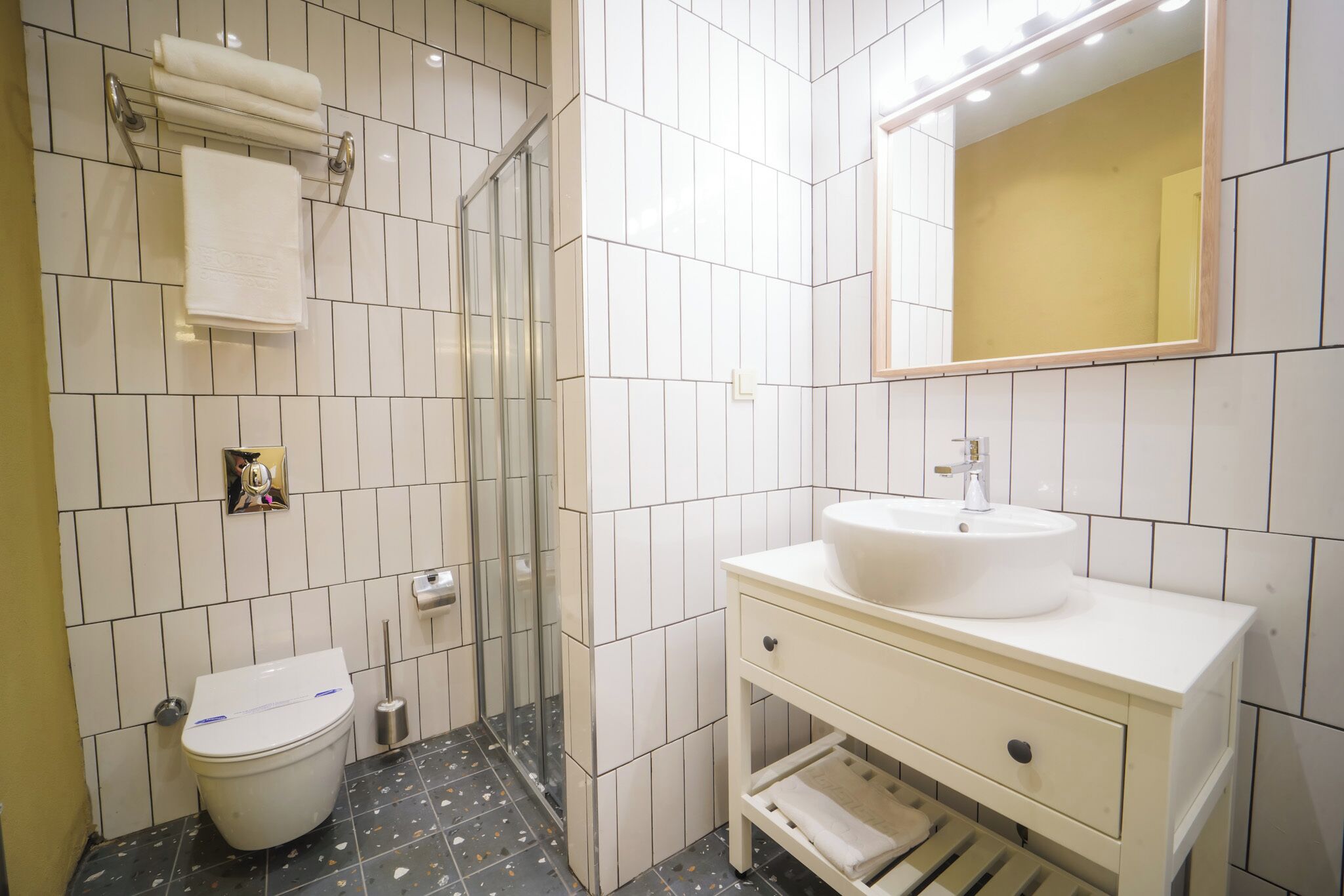 Uma casa de banho moderna com azulejos brancos, sanita, lavatório, espelho e área de duche.