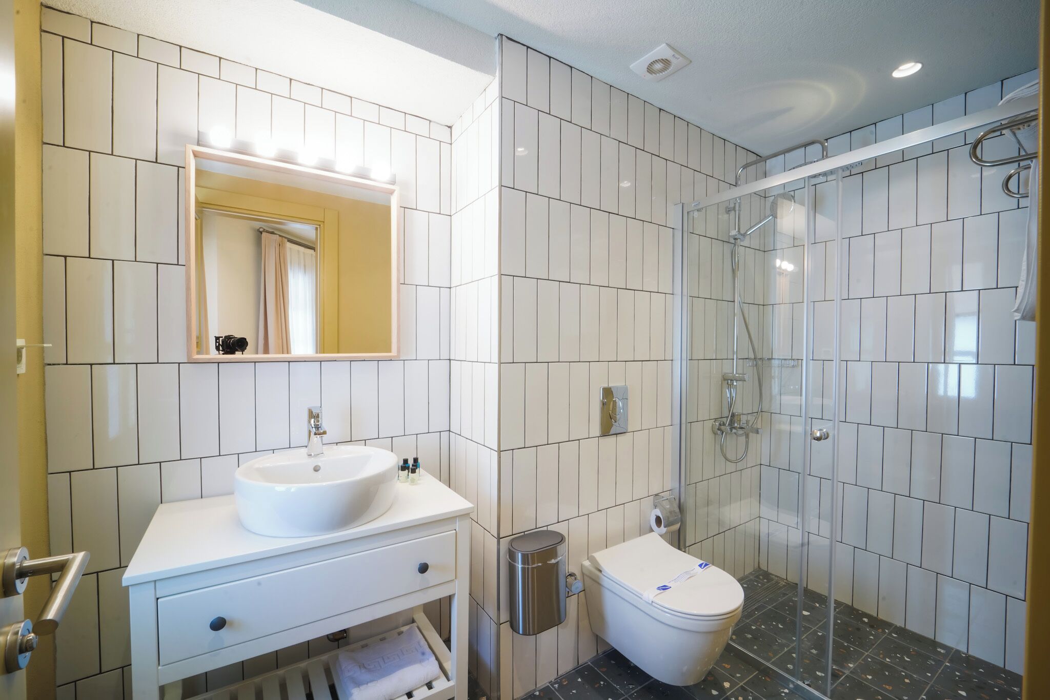 A modern bathroom with a white sink, mirror, and toilet, and a glass-enclosed shower area.