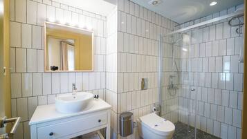 A modern bathroom with a white sink, mirror, and toilet, and a glass-enclosed shower area.