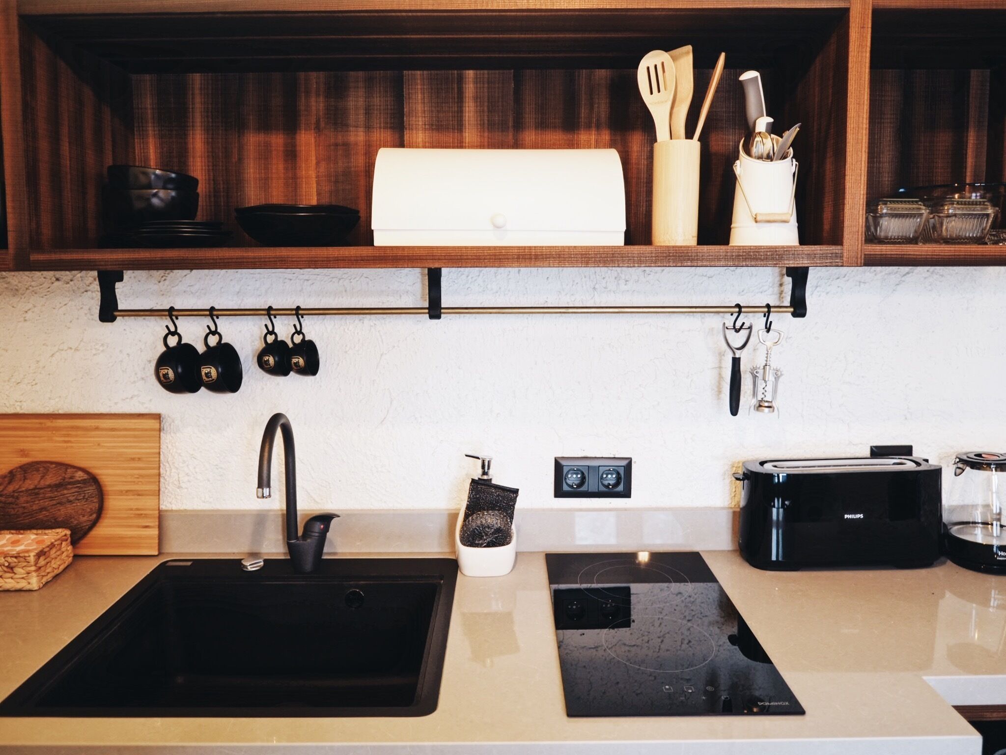 A kitchen with a black sink, a toaster, and a coffee maker. There are hanging kitchen utensils and a spice rack on the shelves.