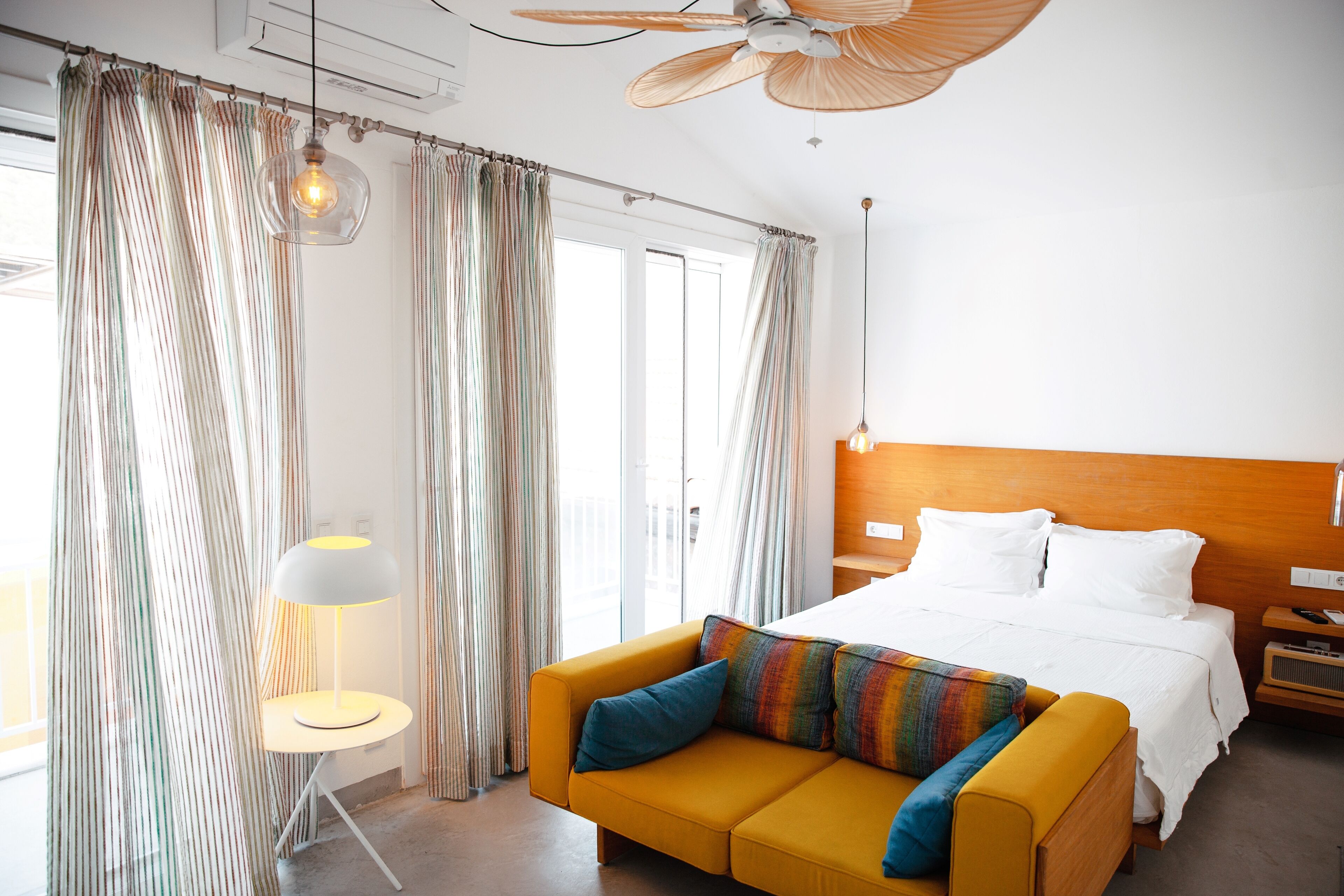 A hotel room with a bed, a yellow sofa, a small table, and a ceiling fan.