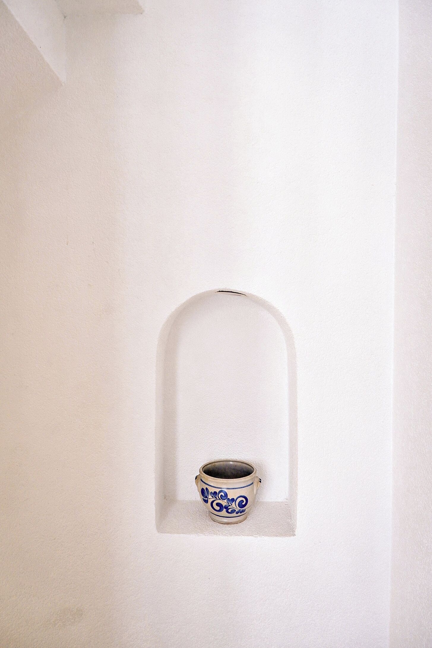 A white wall with a small alcove containing a ceramic mug.